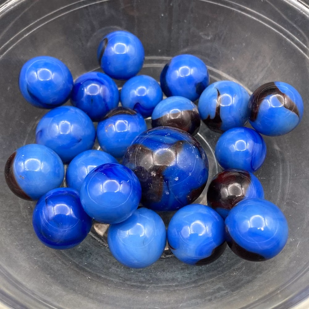 translucent blue glass marbles studio photograph - Sellers reference: marble lot No 25 19 small Marbles, slight variations in sizes. 1 flawed shooter with pitting. Seller isn't an expert on marble types. With research, it appears these are: * Colors: Blue (or Sky Blue) with a translucent Root Beer. The blue shade varies across the marbles. * UV: 365 nm: Minimal Cadmium Glow (Red/Orange). Marbles have some pitting. These are seconds and shapes may be imperfect. Surfaces may not be smooth. Collection sourced from West Virginia. Minimal glowing under strong 365nm. Image show glow under a 365nm spotlight. Does not glow under 395nm. Most standard UV light devices produce UV light that is 395 nm. Listing does not include glass dish or flashlight. Choking Hazard - Contains small parts. Children under 3 yrs. can choke or suffocate on small parts.