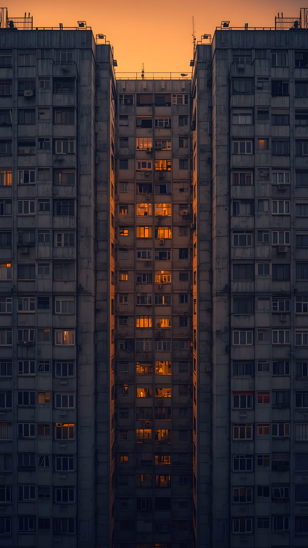 Brutalism aesthetic - Symmetrical view of a residential building at dusk. Warm lights glow in the windows against the dark concrete. A moody look at city life and modern architecture. High-quality vertical aesthetic for your lockscreen.  brutalist architecture, urban windows, city life aesthetic, apartment building light, moody city, dusk photography, symmetrical building, ventanas de la ciudad, arquitectura brutalista, luces nocturnas, edificios de apartamentos, estética urbana, fondos de pantalla oscuros.  #urbanlights #brutalism #citywindows #apartmentliving #moodycity #architecturephotography #nightaesthetic #cityscape #fondosdepantalla #visualsatisfaction #modernbuilding #urbanview